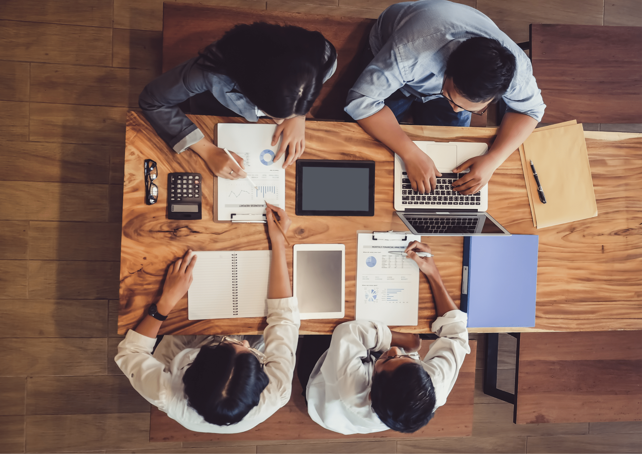 Overhead view of a professional team collaborating with laptops, documents, and data reports on a wooden table.