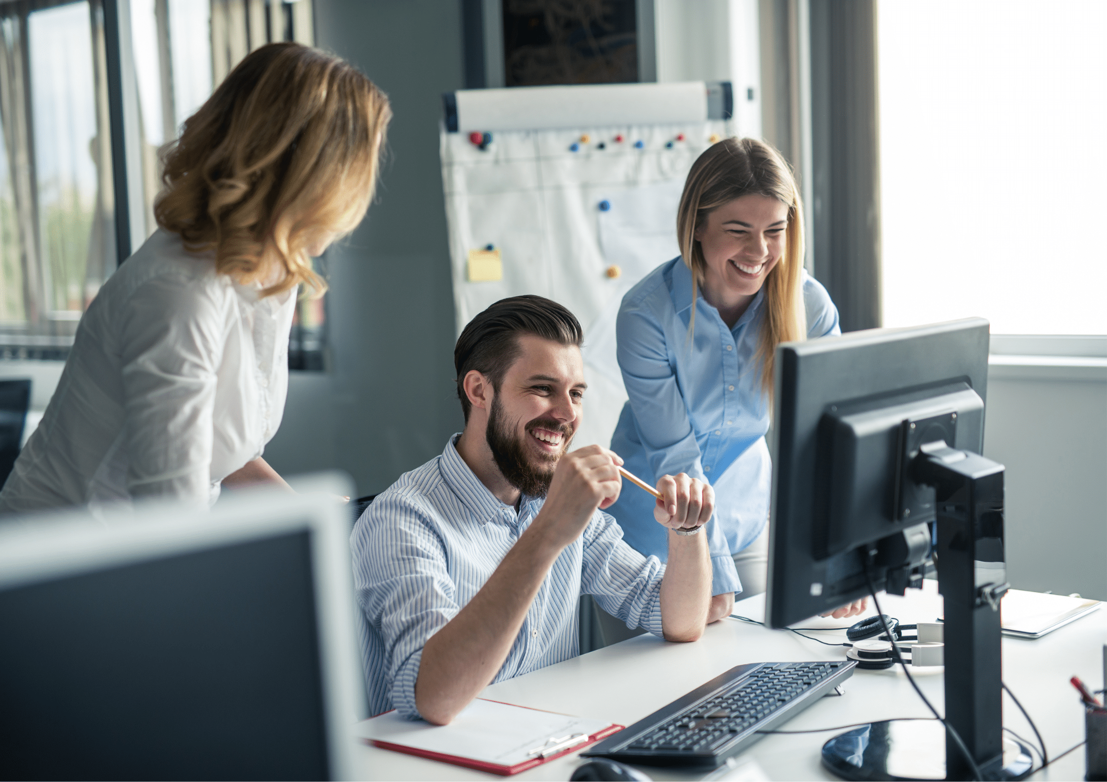 Group of colleagues smiling while collaborating at a computer in a bright, modern office.