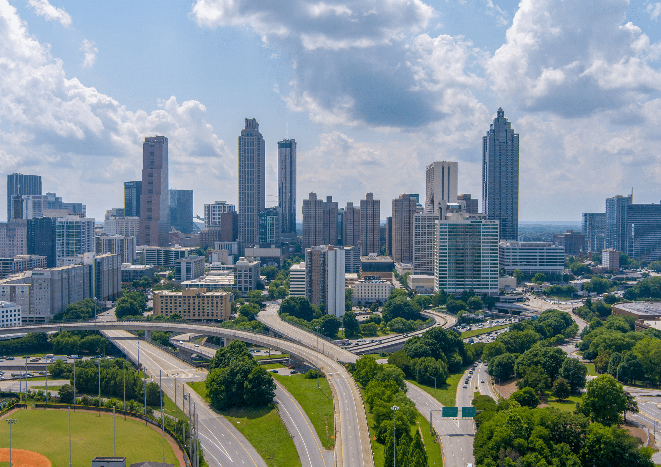 Aerial view of downtown Atlanta skyline with highways and green spaces on a sunny day.