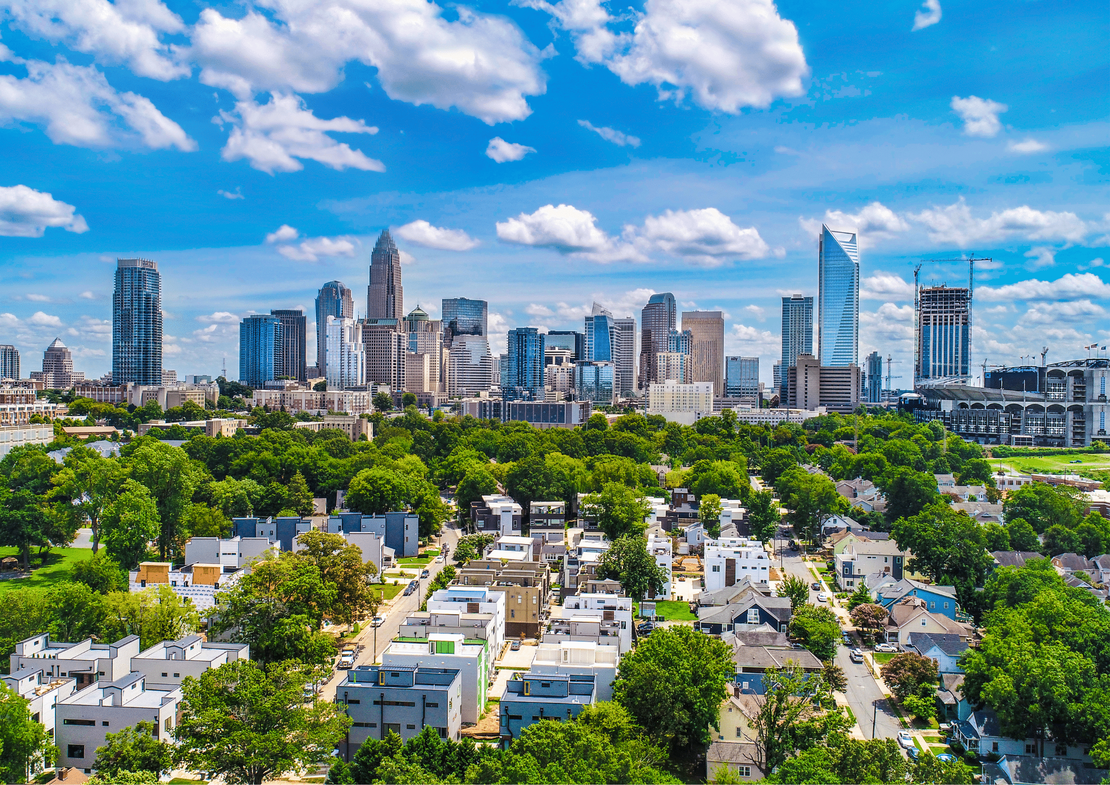 Aerial view of Charlotte, North Carolina skyline surrounded by greenery and residential areas.