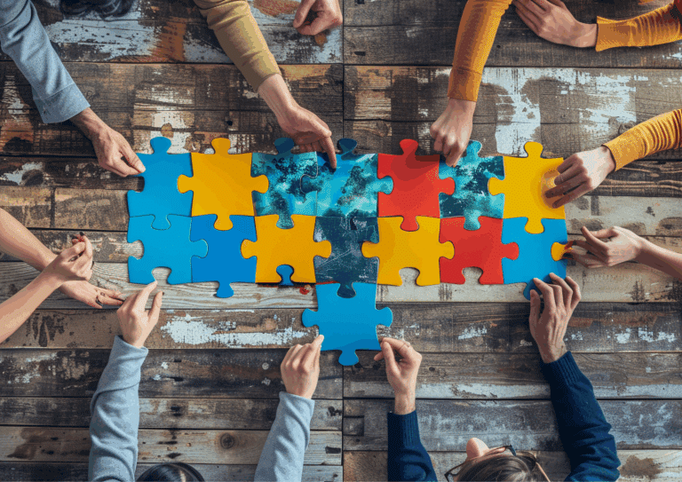 Group of people working together to assemble large, colorful puzzle pieces on a wooden table.