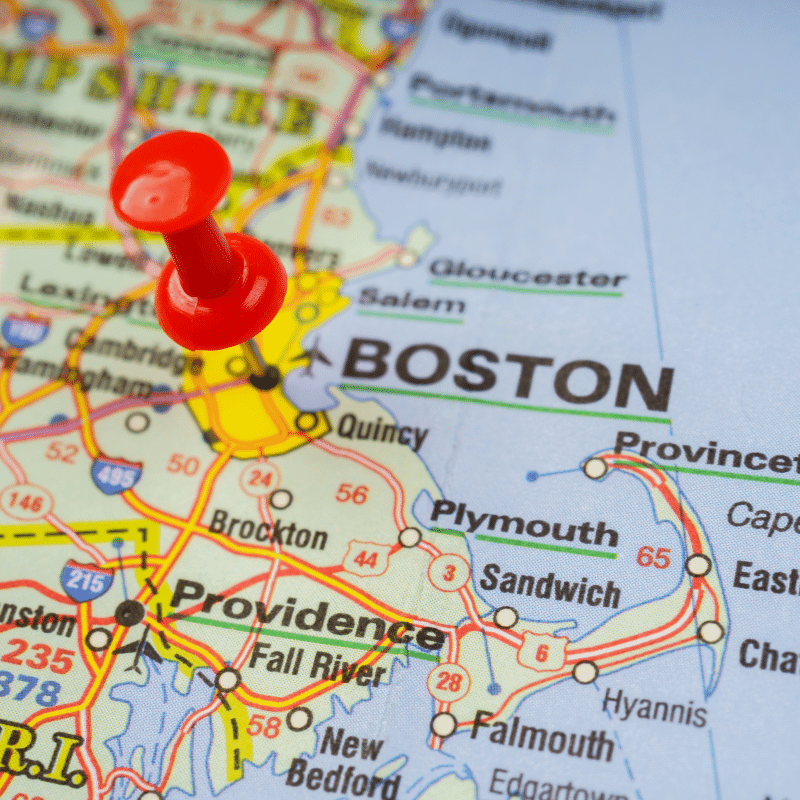 Close-up of a map showing Boston, Massachusetts with a red pushpin marking the city, highlighting its position in the New England region.