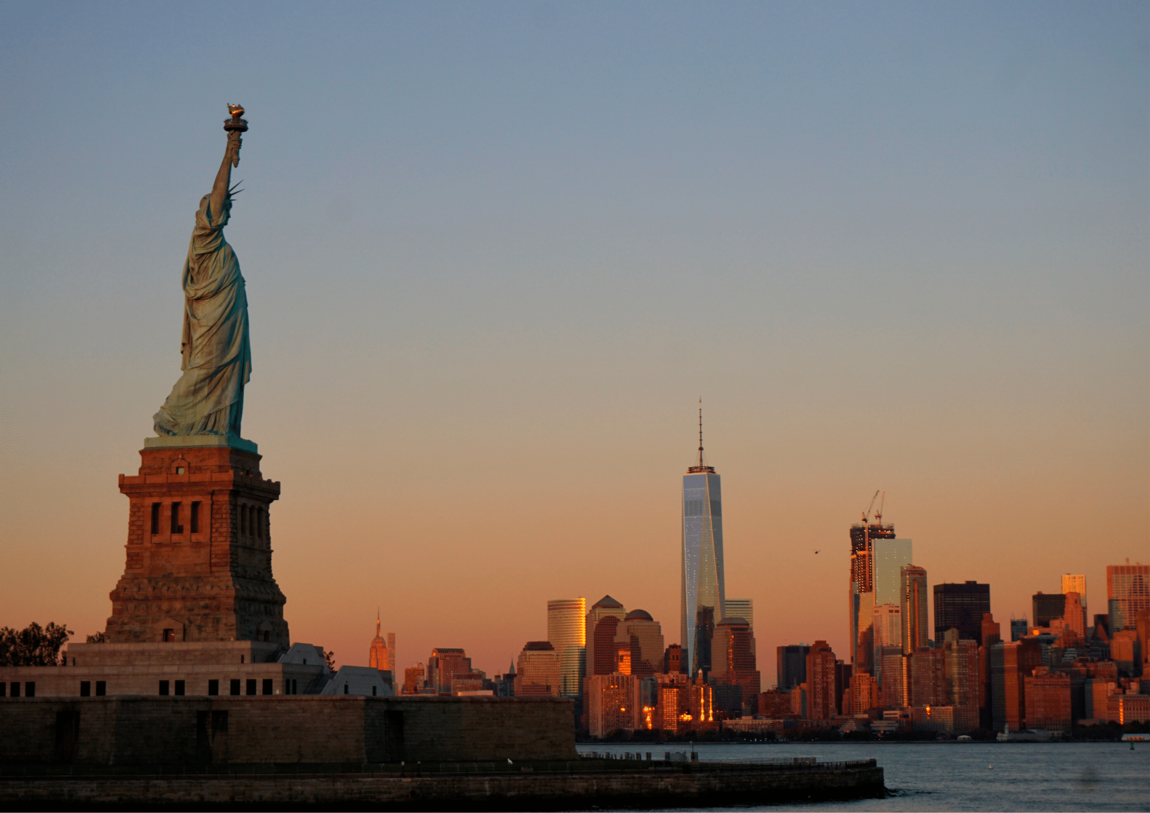 Statue of Liberty with the New York City skyline at sunset, symbolising opportunity and ambition.
