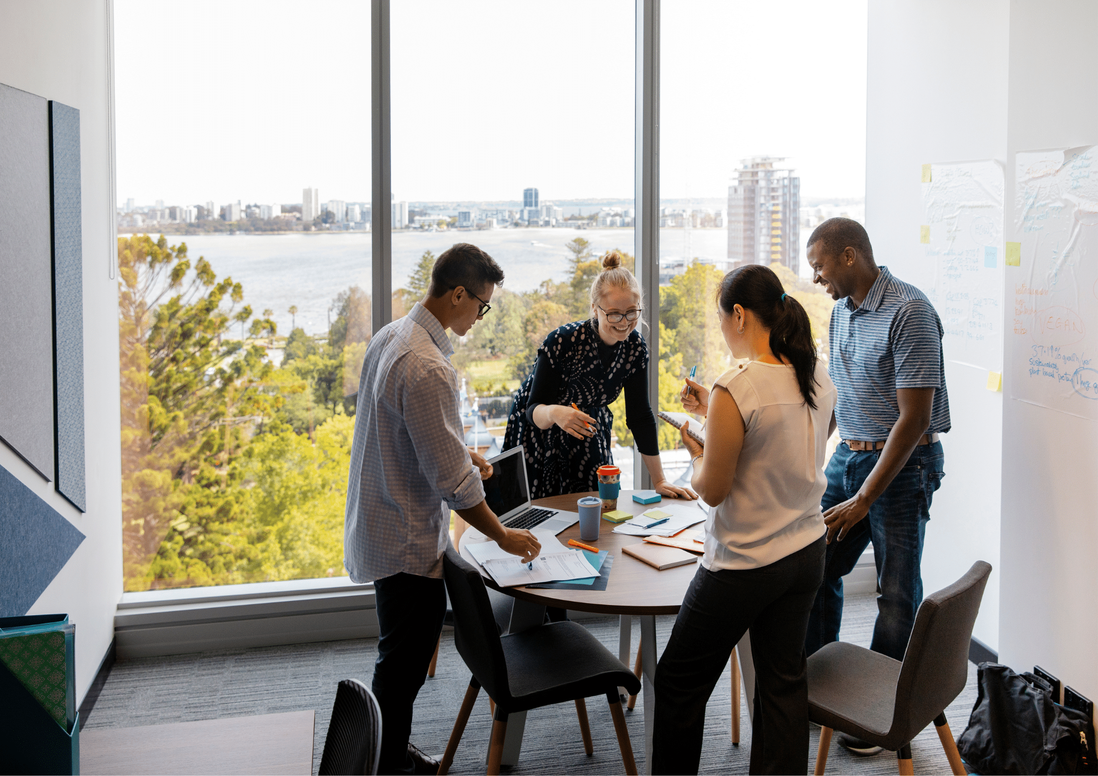 Group of professionals collaborating around a round table in a bright modern office overlooking a city and river, planning strategy and ideas.