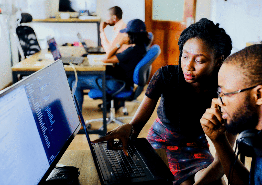 Two software developers collaborating at a desk, reviewing code on a large screen in a modern office environment.