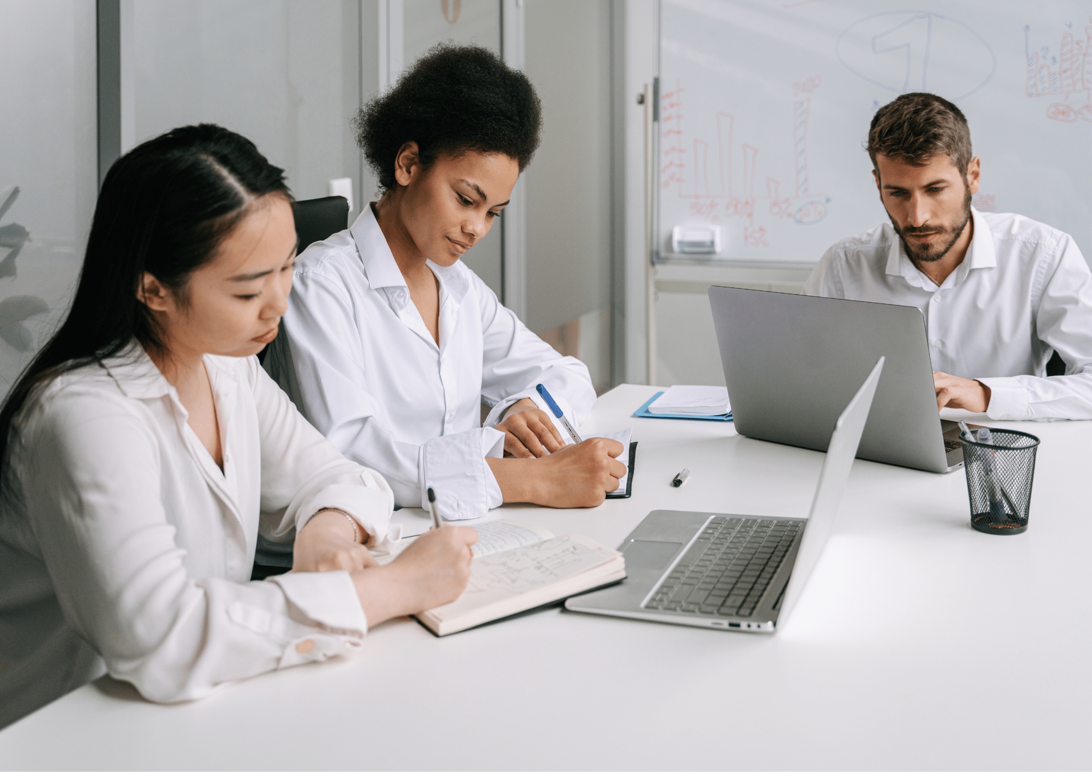 Three colleagues taking notes and working on laptops together in a meeting room