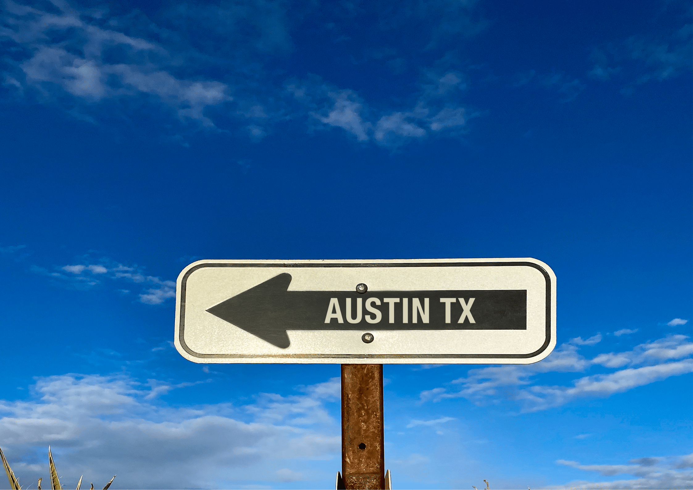 Road sign pointing left toward Austin TX with bright blue sky in the background.